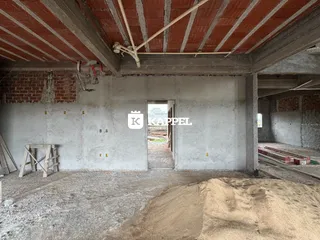 Foto de um espaço interno em construção com paredes de tijolo expostas e estrutura de teto visível.