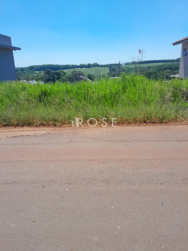 Vista externa de uma propriedade com vegetação verde e estrada de terra no primeiro plano.