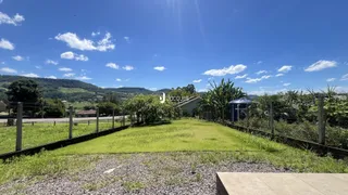 Vista externa de um terreno gramado com cerca e vegetação ao fundo.