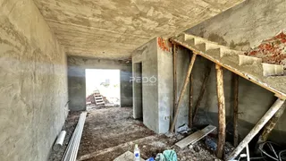 Interior de uma estrutura em construção com paredes de concreto aparente e vigas de madeira expostas.