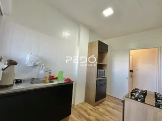 Vista interna de uma cozinha com armários escuros e piso de madeira clara.