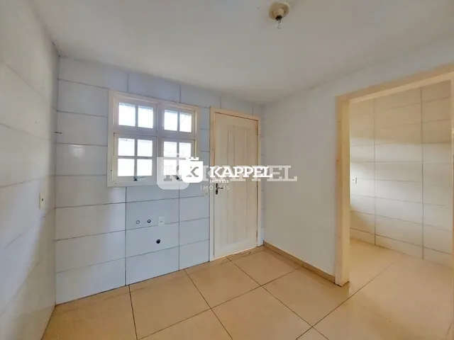 Foto interna de um cômodo com paredes brancas e uma janela.