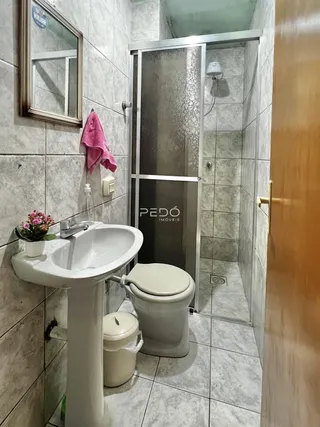 Banheiro com pia de pedestal e box de vidro transparente.