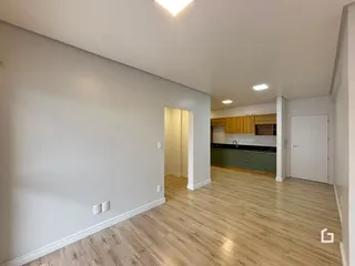 Interior de uma sala de estar com piso de madeira clara e paredes brancas.