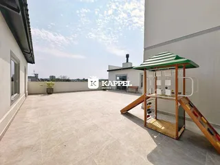 Vista ampla de um pátio externo pavimentado com uma estrutura de madeira ao lado.