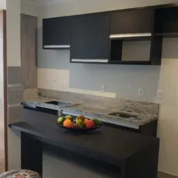 Vista de uma cozinha com armários escuros e bancada de granito.
