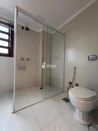 Vista interna de um banheiro com box de vidro e vaso sanitário.