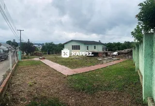 Foto de um terreno com grama e uma residência ao fundo sob um céu nublado.