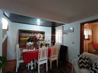 Ambiente interno de uma sala de jantar com mesa redonda e cadeiras brancas.