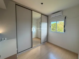 Vista interna de um cômodo com piso de madeira clara e grandes portas de vidro.