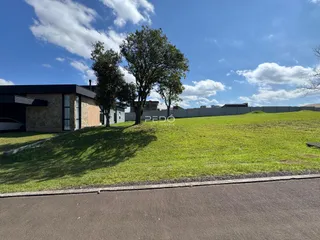 Vista externa da propriedade com gramado e árvores sob um céu azul.
