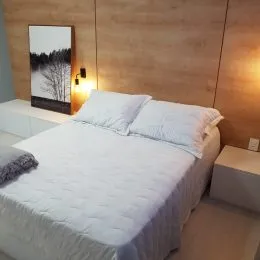 Quarto com cama de casal e parede de madeira clara.
