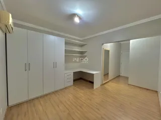 Vista interna de um cômodo com armários brancos e piso de madeira.