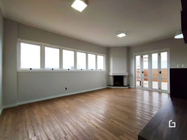Sala de estar com piso de madeira e janelas largas.