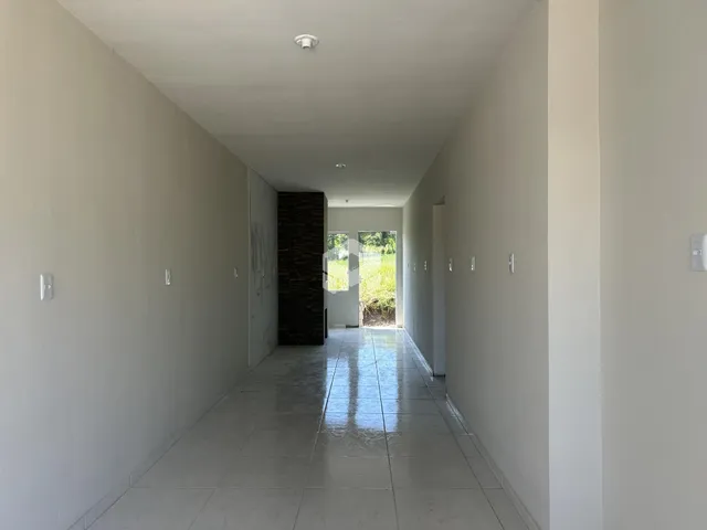 Corredor longo com paredes brancas e piso de cerâmica refletivo.