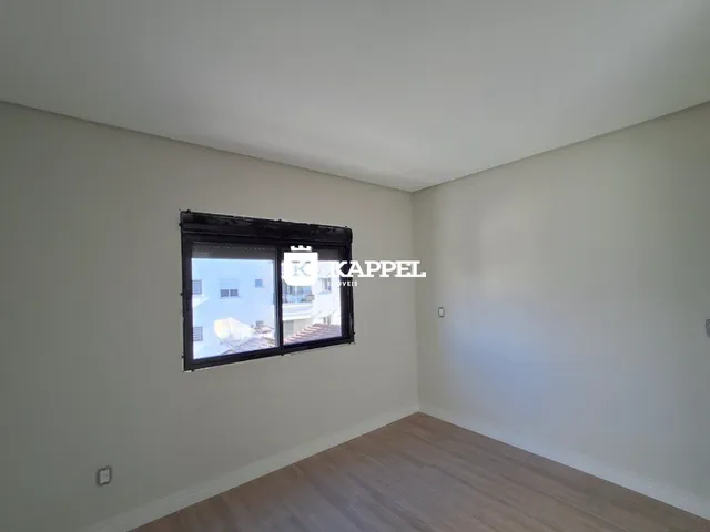 Vista interna de um cômodo com paredes brancas e piso de madeira, mostrando uma janela.