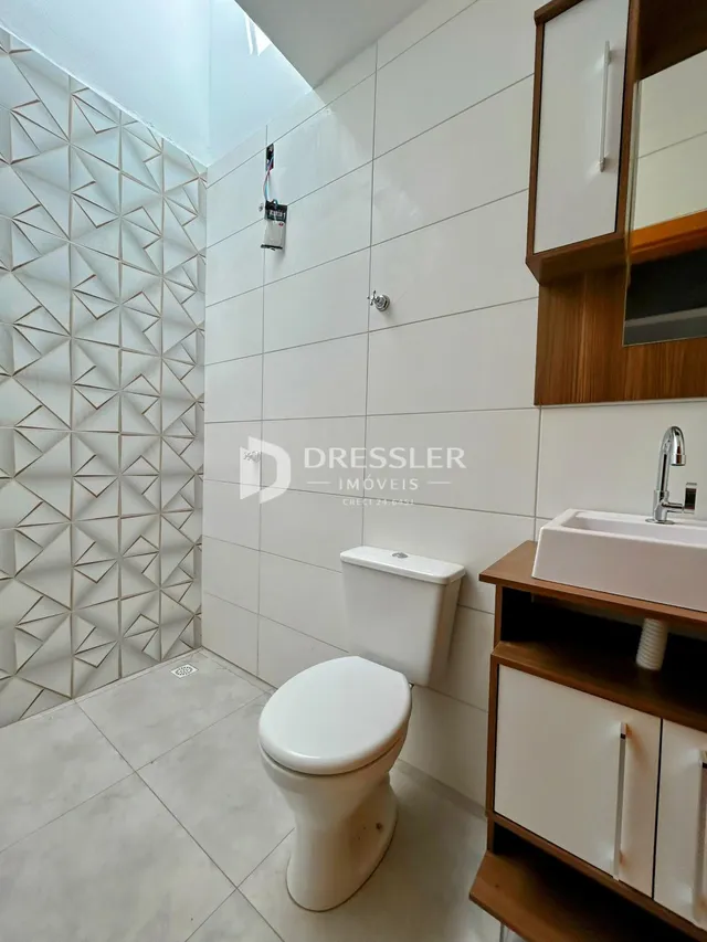 Interior de um banheiro com revestimento de azulejos brancos e louças sanitárias.