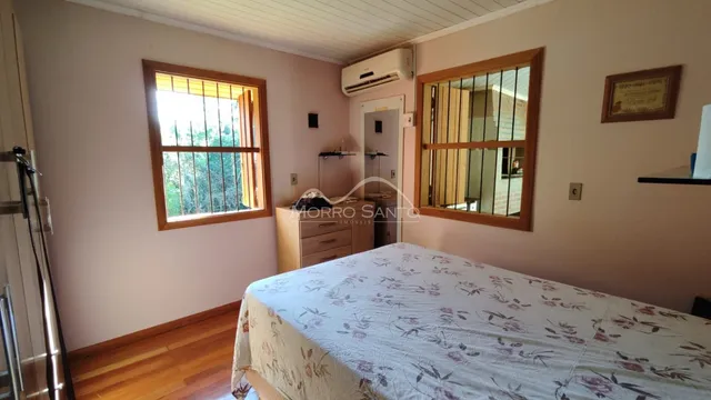 Quarto com cama e janelas em um imóvel com piso de madeira.