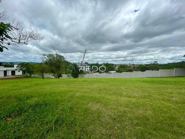 Campo gramado com cerca branca e vegetação ao fundo.