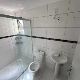 Banheiro com paredes de azulejos brancos e box de vidro transparente.
