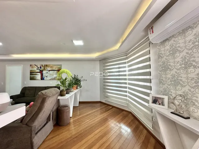 Sala de estar com piso de madeira e cortinas brancas.