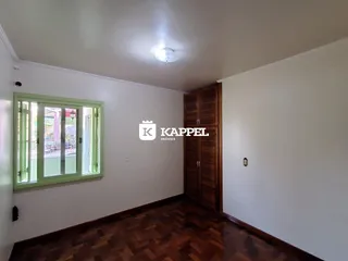 Sala de estar com piso de madeira escura e janela com persianas verdes.