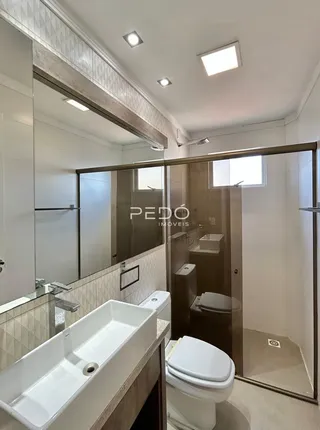 Interior de um banheiro com louças sanitárias brancas e box de vidro.