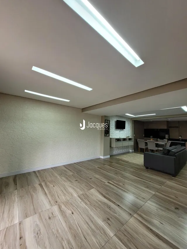 Ambiente interno de uma sala com piso de madeira clara e teto com iluminação em LED.