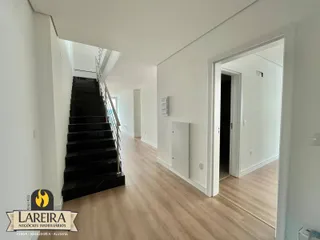 Vista de um corredor com escadaria e piso de madeira clara em um imóvel.