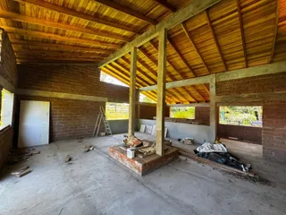 Interior de uma estrutura com paredes de tijolo aparente e teto de madeira em fase de construção.