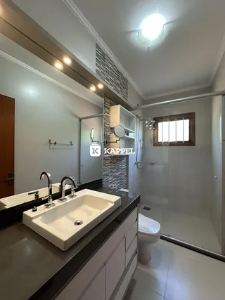 Banheiro com pias duplas e box de vidro transparente.