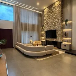 Sala de estar com sofá claro e parede de pedra aparente.