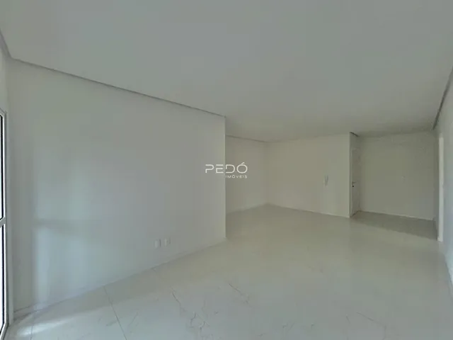 Ambiente interno de uma sala ampla com paredes brancas e piso claro.