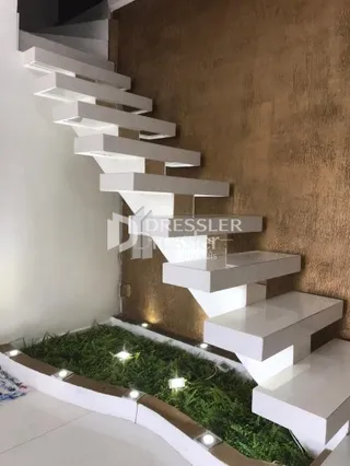Escadaria branca com piso de grama artificial na área comum da residência.