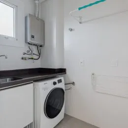 Foto de uma área de lavanderia com máquina de lavar e bancada escura.