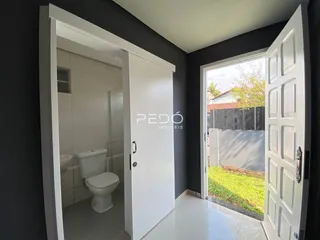 Vista de um corredor interno com acesso a um banheiro e porta de vidro.