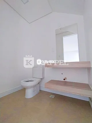Foto interna de um banheiro com vaso sanitário branco e prateleira de madeira.