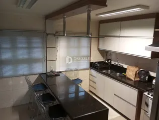 Vista interna de uma cozinha com armários brancos e bancadas escuras.
