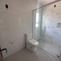 Banheiro com revestimento de azulejos brancos e box de vidro transparente.
