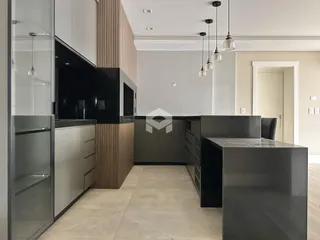 A cozinha moderna apresenta armários escuros e iluminação pendente.
