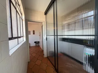 Hall de entrada com piso de terracota e divisória de vidro.