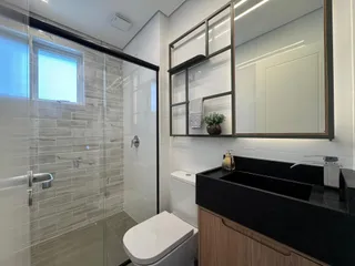 Banheiro com box de vidro e bancada escura.