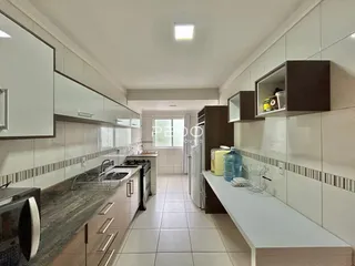 Vista interna de uma cozinha com revestimentos brancos e armários escuros.
