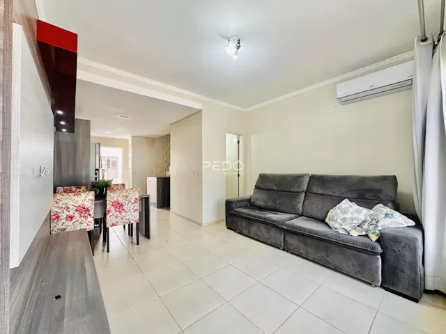 Sala de estar com sofá cinza e piso de cerâmica clara.