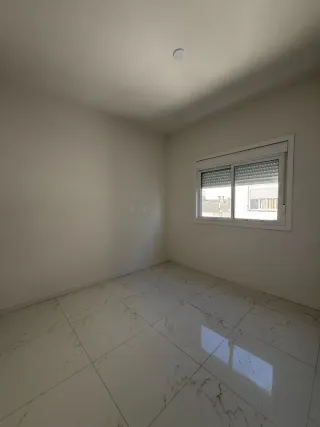 Sala de estar com piso de porcelanato claro e janela na parede.