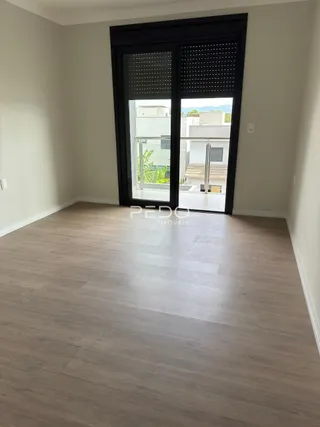 Vista interna de um cômodo com piso de madeira clara e porta de vidro escura.