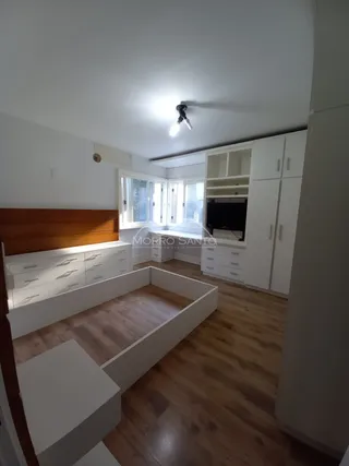 Quarto com cabeceira e armários embutidos brancos.