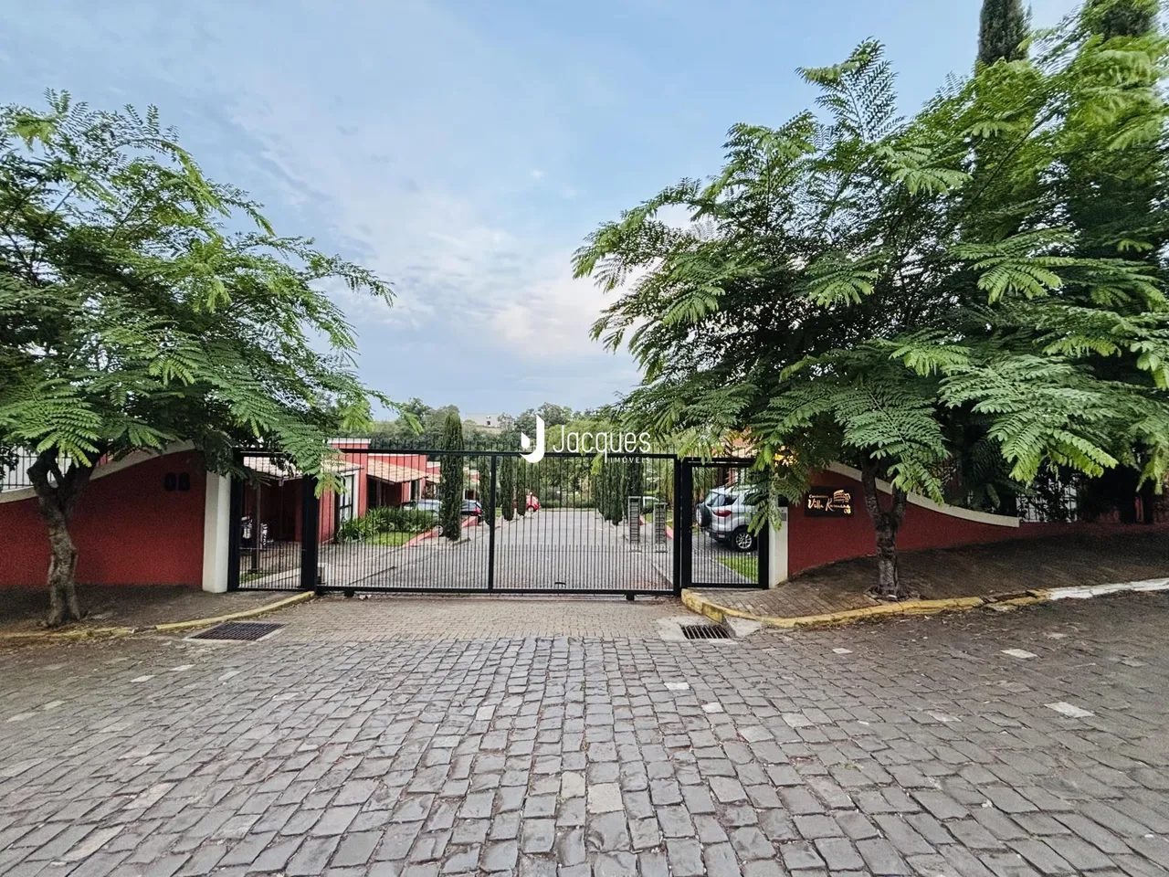 Vista da entrada de uma propriedade com portão de ferro e vegetação.
