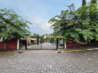 Vista da entrada de uma propriedade com portão de ferro e vegetação.