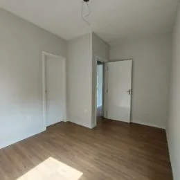 Foto interna de um ambiente com piso de madeira e paredes brancas.
